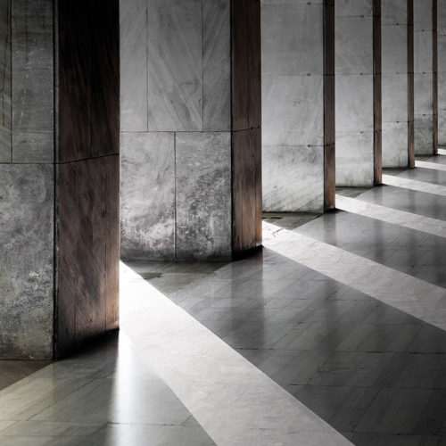 Row of columns with sunlight in the gaps and reflected in shiny floor