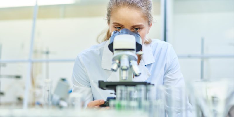 Woman in white lab coat looking into microscope